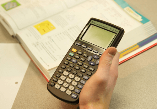 Hand holding a graphing calculator with a math book in the background.