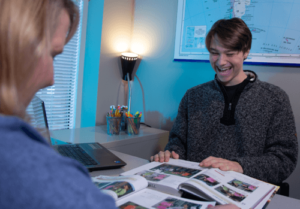 Student and teacher laughing while looking at open books on a table.