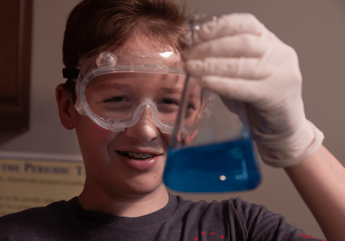 Student wearing goggles and holding a beaker while in science class.