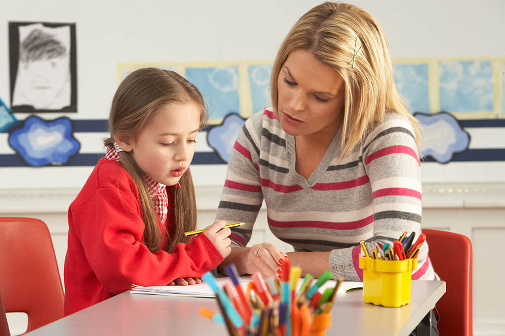 Teach sitting with a young female student while looking at a tablet.