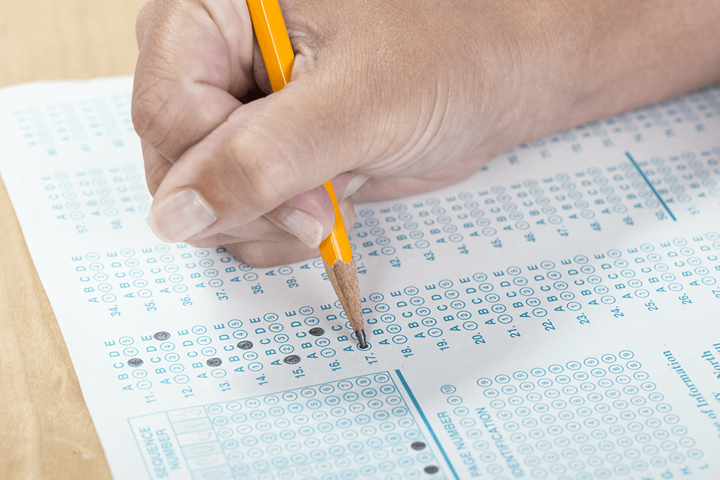 Hand holding a pencil while filling in an answer on a test.